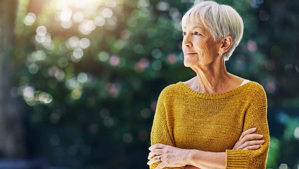 Relaxed woman with arms crossed standing in a garden