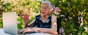 Older lady sat at garden table typing on a laptop