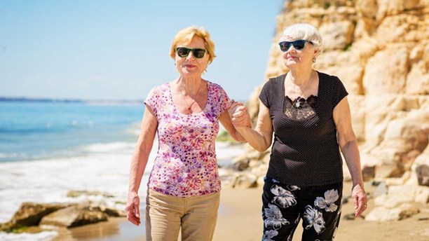 Older female couple walking holding hands on the beach