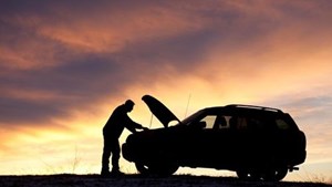 Broken down car with open bonnet and person looking at the engine during sunset