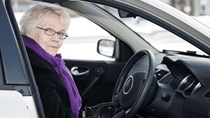 An older woman sits in the driving seat of a car.