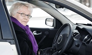 An older woman sits in the driving seat of a car.