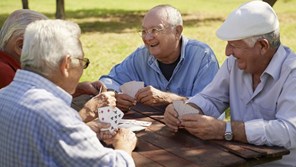 A group of elderly men outside laughing outside on picnic bench