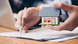 Person reviewing documents on a desk and holding a model house