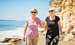 Older female couple walking together along a beach holding hands